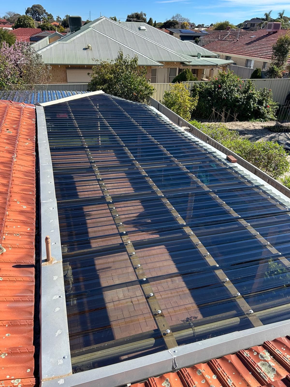 New clear polycarbonate roof sheeting run the length of a patio, flashed into the terracotta tiled roof alongside it
