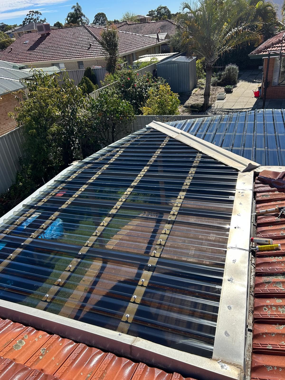 New patio roof sheeting meeting an existing tiled roof, with fresh ridge capping and flashing along the join